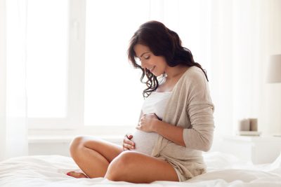 woman sitting on her bed, rubbing her pregnant belly and smiling