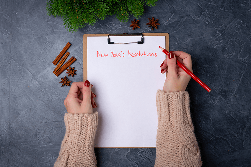 Woman hands ready to write new year's resolutions on blank list on dark background.