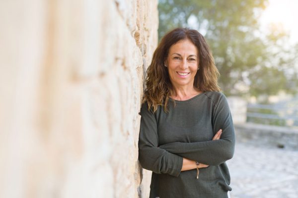 mature adult woman smiling with teeth and leaning against a wall