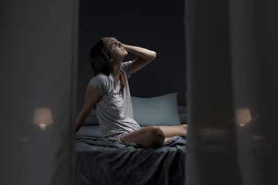 adult woman awake at night and sitting on her bed with headache