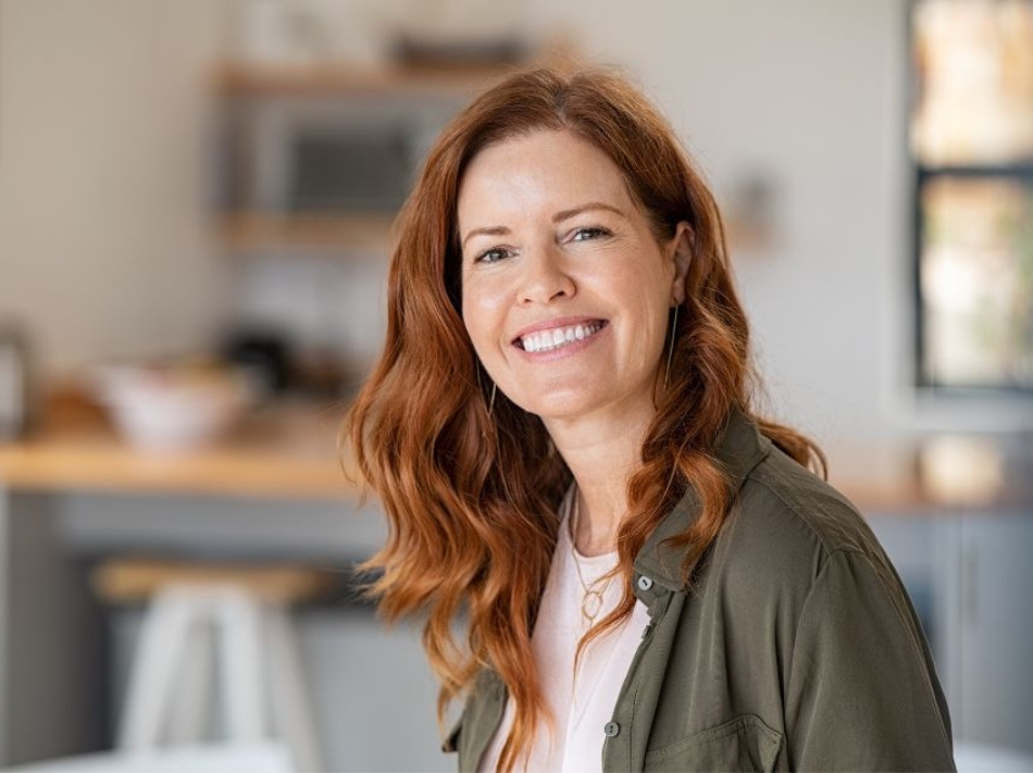 A woman with long, red hair sitting and smiling